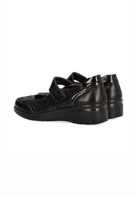 Zapatos de cuero negro con un acabado brillante, que presentan un patrón texturizado, un cierre de tira de Velcro y un tacón bajo en cuña.