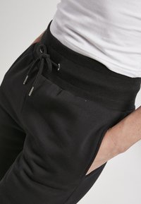 Schwarze Jogginghosen mit einem gerippten Bund, verstellbarem Kordelzug und Seitentaschen. Der Stoff wirkt weich mit einer glatten Textur.