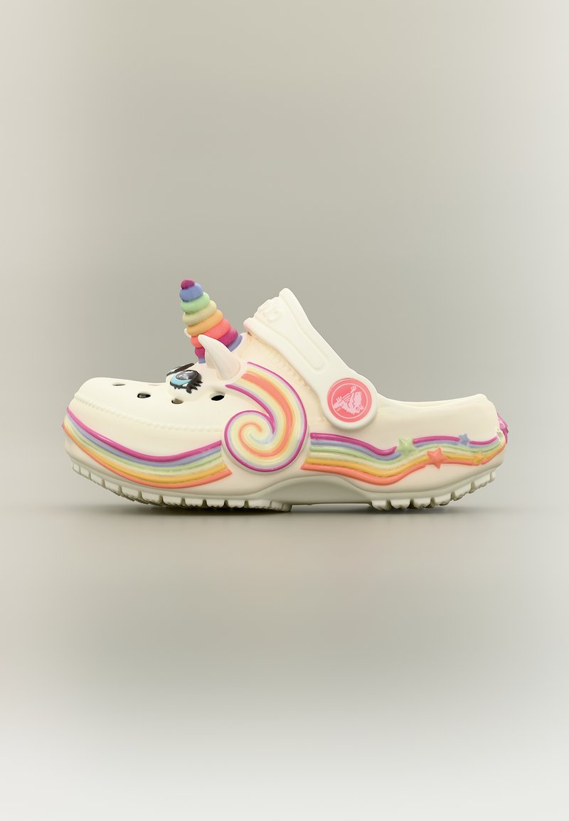 Chaussure blanche style sabot avec une corne de licorne arc-en-ciel, une oreille, une décoration en forme d'œil, et des rayures arc-en-ciel colorées avec des accents d'étoiles sur les côtés.