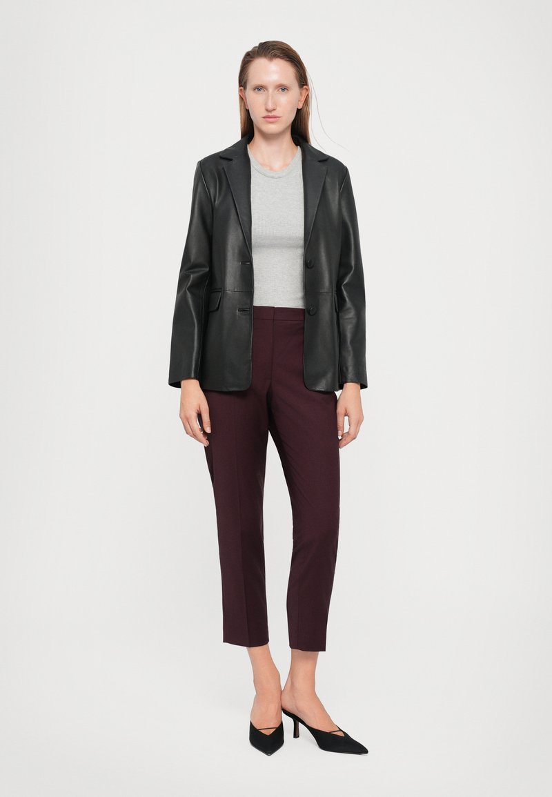 Zwarte neplederen blazer over een grijze top, gecombineerd met bordeauxrode tapered broek en zwarte puntige hakken. Glad textuur en aansluitend ontwerp.