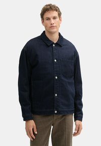 Dunkel marineblaue Jeansjacke mit Kragen, Knopfleiste vorne und aufgesetzter Tasche. Mit langen Ärmeln und entspanntem Schnitt.