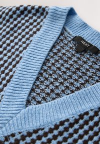 Pull en maille col en V avec bordure côtelée bleu clair et motif texturé marron et bleu, comprenant une étiquette noire avec le texte "NEXT".