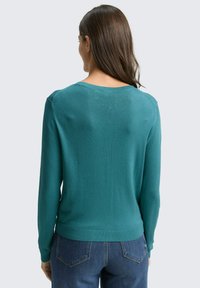 Turkusowy dzianinowy sweter z długimi rękawami, okrągłym dekoltem i zakończeniem na ściągaczu. Gładka faktura, dopasowany fason, noszony z niebieskimi jeansami, widok od tyłu.