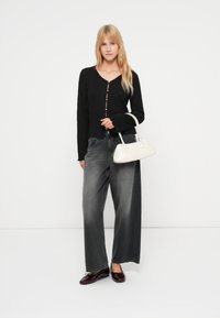 Μαύρη πλεκτή ζακέτα με V-λαιμόκοψη και κουμπιά, συνδυασμένη με γκρι τζιν παντελόνι φαρδύ στο πόδι. Άσπρη τσάντα χειρός και μπορντό παπούτσια ολοκληρώνουν το σύνολο.