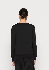 Sudadera negra de manga larga con cuello redondo, costuras fruncidas en los hombros, tejido suave y puños elásticos en las muñecas y el dobladillo.