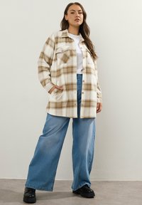 Ruudullinen takki vaaleassa ja beigessä, jossa on nappisuljenta, rintatasku ja sivutaskut, yhdistettynä vaaleansinisiiin leveälahkeisiin farkkuihin.