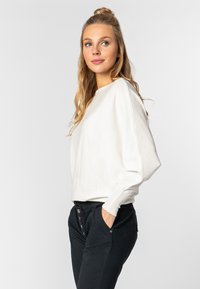 Witte lange mouwen top met een ronde halslijn en verlaagde schouders, gecombineerd met zwarte broeken met knoopdetails en zijzakken.