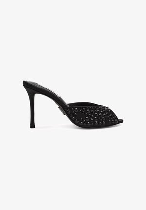 Zueco negro de tacón alto con punta abierta, decorado con tachuelas negras brillantes en la parte superior.