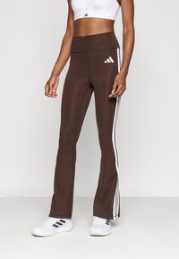 Leggings marron évasés avec des bandes blanches sur les côtés et une taille haute. Fabriqués dans un tissu extensible, conçus pour le confort et la liberté de mouvement.