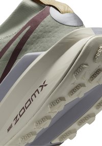 Gros plan de la semelle d'une chaussure de course Nike ZoomX gris et beige avec des reliefs texturés et des accents bordeaux sur le côté et la languette du talon.