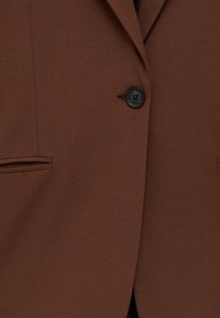 Blazer marron avec un seul bouton noir fermé, doté de deux poches horizontales fendues près de la taille.