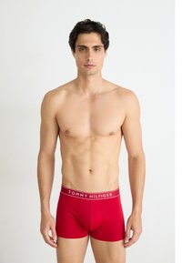 Piros pamut boxer sort fehér "TOMMY HILFIGER" márkázott derékkal, illeszkedő fazonban és sima textúrával, férfi modellen bemutatva.