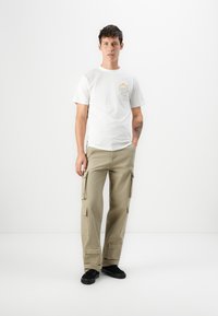 Hvid bomulds t-shirt med rund hals og lille multifarvet print. Lyse khaki cargo bukser med sidelommer, og sorte sko.
