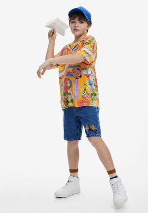 Colorful short-sleeve shirt with various prints, denim shorts with a butterfly patch, and white high-top sneakers. Blue cap and paper airplane.