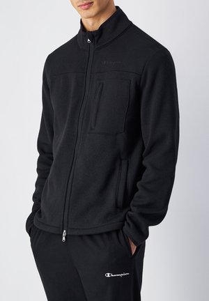 Schwarze Fleecejacke mit hohem Kragen, Reißverschluss und Fronttasche. Enthält das Champion-Logo auf der Brust und passende schwarze Hosen.