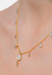 Collier en or avec des pierres claires en forme de goutte d'eau, chaîne texturée et un pendentif central mettant en vedette une pierre plus grande sertie dans un contour décoratif.