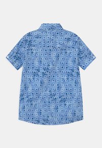 Camicia azzurra a maniche corte con bottoni, decorata con un motivo geometrico simile a fiori bianchi e blu scuro, vista da dietro.