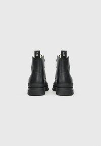 Botas de cuero negro hasta el tobillo con un acabado texturizado, que cuentan con una suela negra robusta y una lengüeta con la etiqueta "CPH" en la parte trasera.