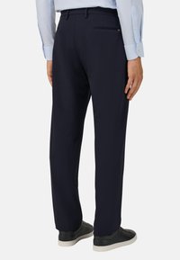 Granatowe spodnie wykonane z gładkiego materiału, z zamykanym na zamek tylnym kieszeniem i prostym krojem nogawek, zestawione z czarnymi sneakersami.