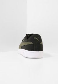 Zapatilla negra y verde oliva con un acabado de cuero suave, suela de goma blanca y un discreto detalle del logo en el talón.