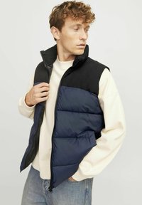Puffa veste ar melno augšējo un tumši zilā apakšējā daļu, ar rāvējslēdzēju un kabatu kreisajā pusē; mīksta, quilted tekstūra.