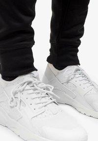 Scarpe sportive bianche realizzate in materiali misti di rete e pelle, con punte arrotondate, suola texturizzata e più occhielli stringati con lacci bianchi piatti.