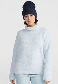 Lichtblauwe fleece trui met een hoge kraag en lange mouwen, met een gestructureerd oppervlak. Gecombineerd met een donkerblauwe gebreide muts.