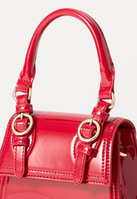 Sac à main en cuir verni rouge au design structuré, avec des accessoires en or, des anses en boucle et des détails de couture précis.