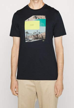 Maglietta nera a maniche corte con una grafica colorata di Palm Springs, California, indossata da una persona con pantaloni beige, mostrata dalla nuca fino a metà coscia.
