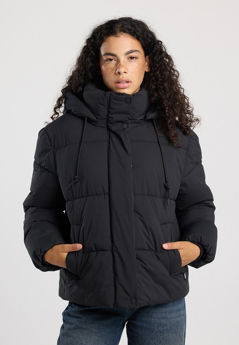 Veste noire matelassée avec un col haut, cordons de serrage réglables, boutons-pression et poches latérales ; elle présente un design matelassé et une texture douce.