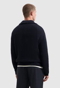Marineblauwe geribde trui met kraag, textuurstof en aangesloten ontwerp. Heeft een lichte drop shoulder en een ontspannen silhouet.