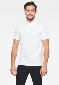 Vit kortärmad polo med krage, tvåknapplås och subtilt logodetalj. Slät tyg och figurnära design.