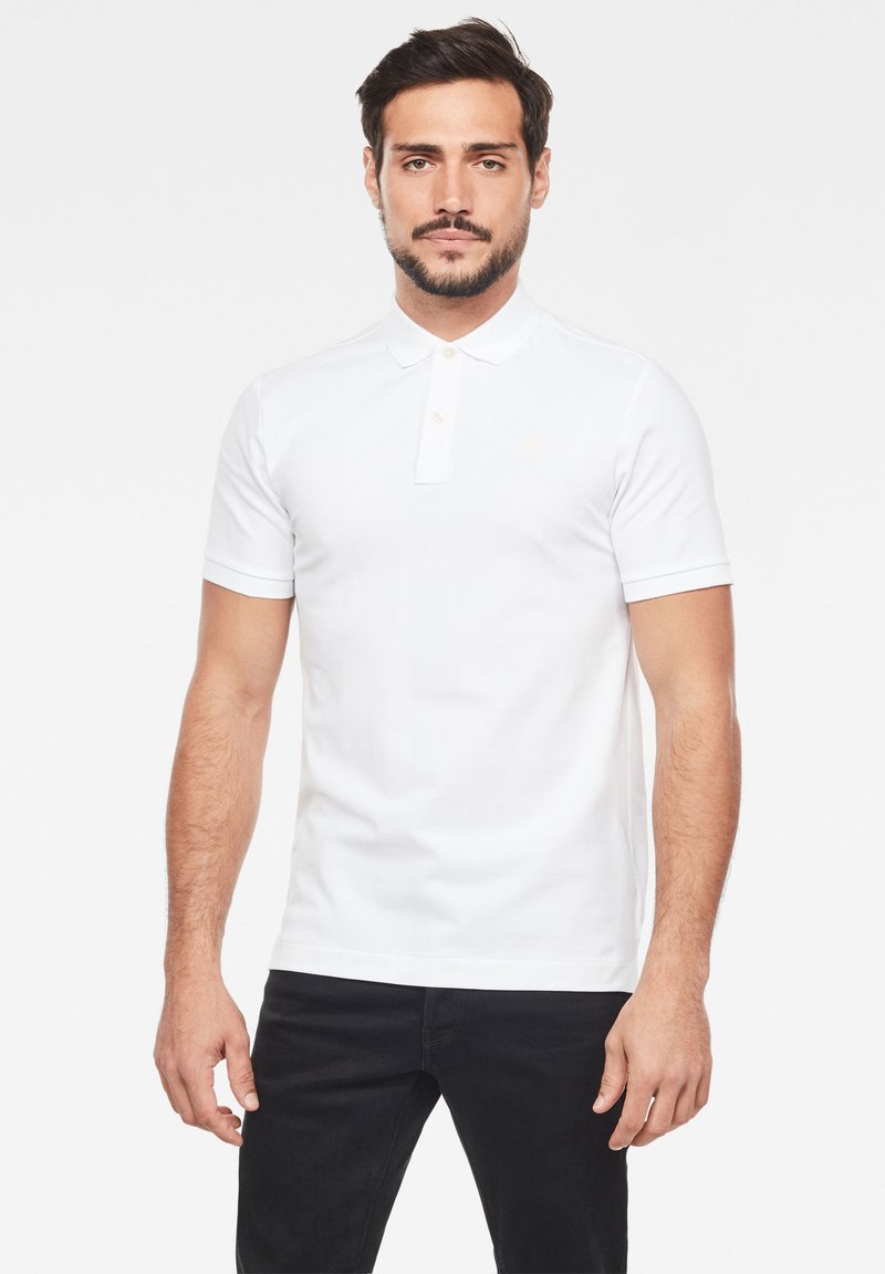 Vit kortärmad polo med krage, tvåknapplås och subtilt logodetalj. Slät tyg och figurnära design.