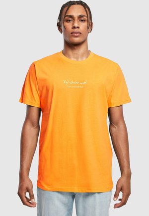 Orange Baumwoll-T-Shirt mit arabischem und englischem Text "Love yourself first" auf der Brust, kurzen Ärmeln und einem lässigen Schnitt.