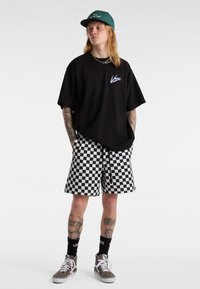 Black oversized t-shirt with a white logo, checkered black and white shorts, and gray high-top sneakers with white accents.