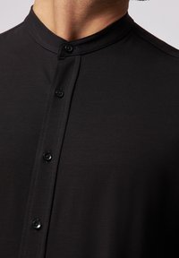 Camisa negra de botones con cuello mao, que presenta una textura suave, pequeños botones redondos y un diseño elegante y moderno.