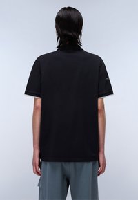 Camicetta nera a maniche corte con vestibilità rilassata, caratterizzata da un design semplice e dettagli grigi evidenti sul colletto e sulle maniche.