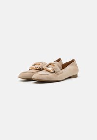 Beige suède loafers met ronde neuzen en een platte hak, met een grote goudkleurige metalen accent aan de voorkant en gestikte details.