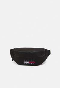 Black waist bag with two zippered compartments and a "Tommy Outdoors Jeans" logo patch on the front center.