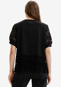 Černý top s krátkým rukávem, krajkovými rukávy, třásněmi na spodním lemu a texturovanými detaily na zadní straně. Měkký materiál s jemným krajkovým vzorem na rukávech.