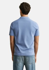 Vaaleansininen lyhythihainen polo-paita, jossa on ribbauskaulus, sileä pinta ja suora helma, yhdistettynä vaaleisiin farkkuihin.