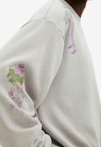Sudadera gris hecha de una tela suave, con ilustraciones estilo acuarela en ambas mangas con colores pastel y diseños divertidos.