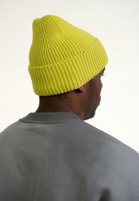 Gorro de punto en un vibrante color amarillo con textura acanalada, mostrado desde la parte de atrás, combinado con un suéter gris de cuello redondo.