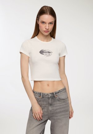 T-shirt bianca a maniche corte con stampa di labbra grigie e testo "Kiss Me, Maybe?" abbinata a jeans grigi sbiaditi a vita alta.