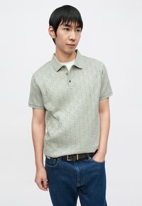 Ανοιχτό πράσινο πόλο πουκάμισο με υφή διαμαντένιου μοτίβου, τριπλό κουμπωμα και κλασικό γιακά, σε συνδυασμό με μπλε τζιν και μαύρη ζώνη.