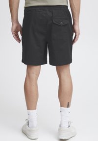 Shorts noirs avec une taille élastique, dotés d'une poche arrière avec bouton, d'une coupe jusqu'aux genoux et d'un tissu en coton lisse.