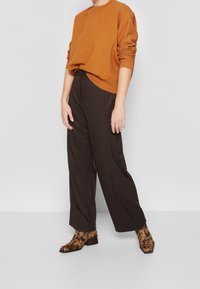 Brown oversized sweatshirt, tailored dark trousers, and patterned brown ankle boots with a square toe. Simple, relaxed fit and textures visible.