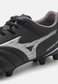Crampon de football noir en cuir synthétique avec des accents gris, une surface texturée, un design incurvé et un détail de logo argenté distinctif.