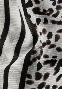 Tissu blanc à rayures verticales noires et taches léopard irrégulières noires et marron, présentant une surface texturée légèrement froissée.