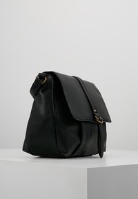 Borsa nera in pelle con pattina pieghevole, tracolla regolabile e dettagli in metallo dorato. Finitura testurizzata, corpo spazioso, design minimalista.